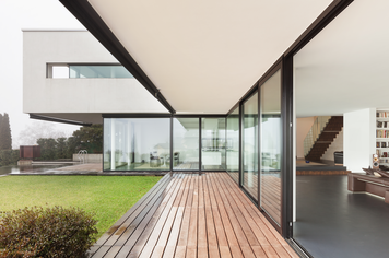 Eine Terrasse aus der Außenansicht. Viele aneinandergereihte Terrassenfenster und eine offene Terrassenschiebetür. 