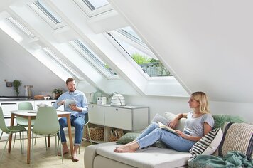 Ein Mann und eine Frau in einem modernen Zimmer und drei Dachfenster, wovon eines geöffnet ist. 