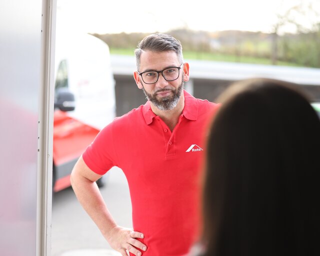 Ein Mann mit rotem Roto-Polo, dem die Eingangstür geöffnet wird.  