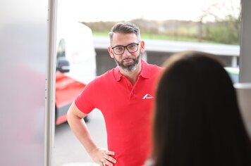 Ein Mann mit rotem Roto-Polo, dem die Eingangstür geöffnet wird.  