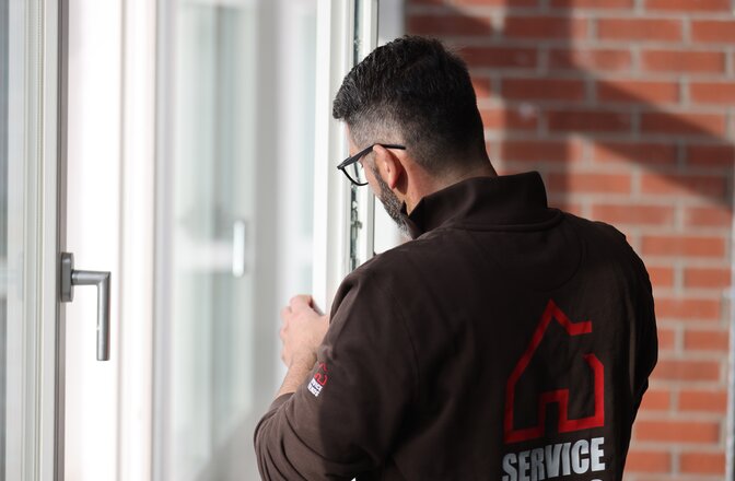 Ein Mann aus der Perspektive von hinten. Er hält und schaut auf ein Fensterflügel von einem offenen Fenster.