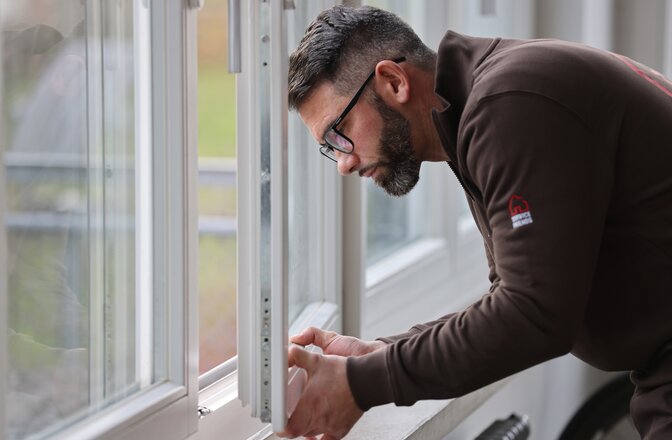Ein Mann von der Seitenperspektive, der ein Fensterflügel eines offenen Fensters festhält.