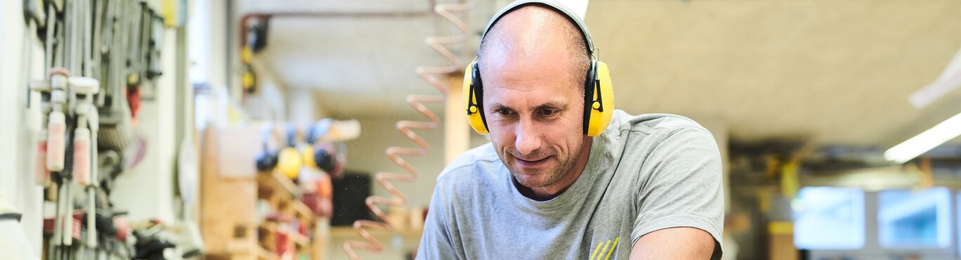 Ein Mann in einer Werkstatt der seine Hände auf einem Holzbalken abstützt.